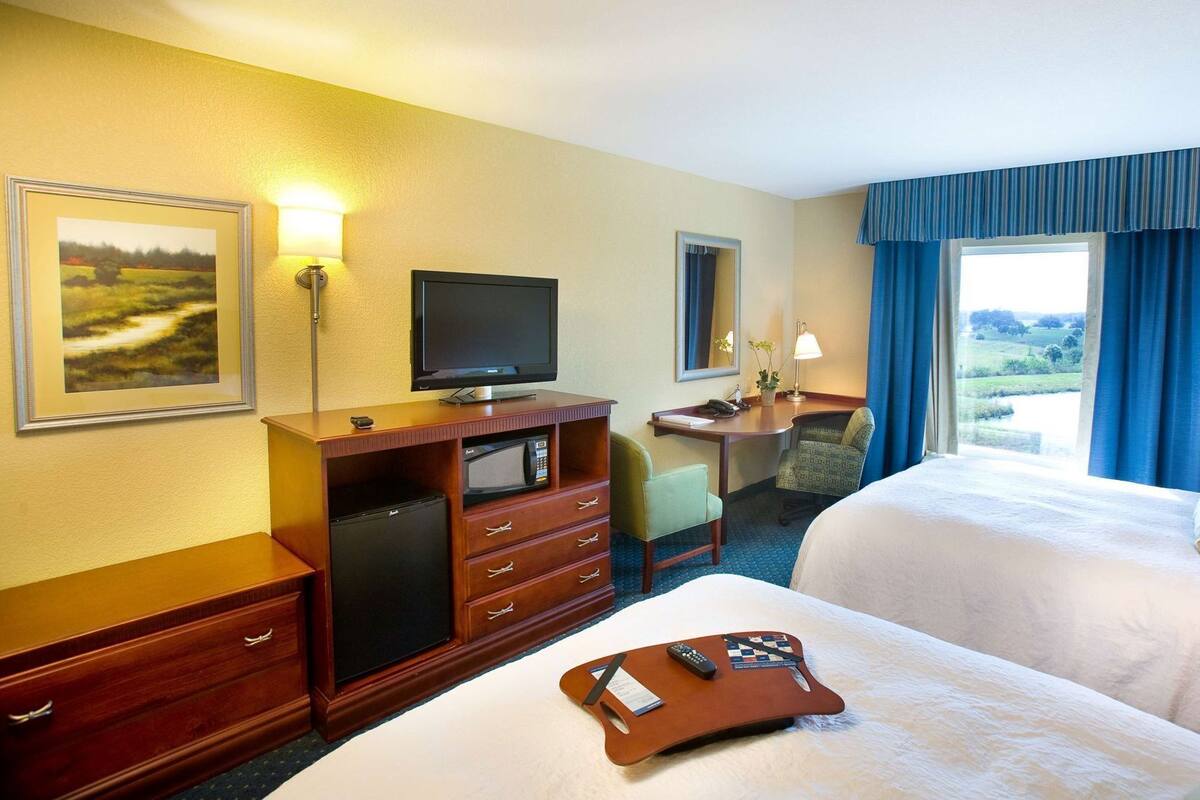 A hotel room with a bed, a desk with a computer, a television, and a window with curtains.