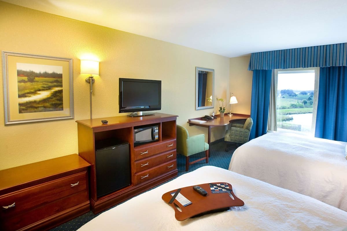 A hotel room with a bed, a desk with a computer, a television, and a window with curtains.