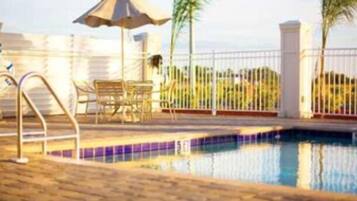 A swimming pool with a metal ladder, a lounge chair, and a table.