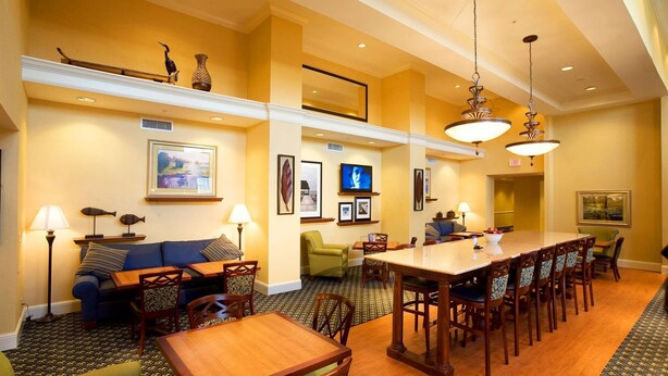 A hotel dining area with a long wooden table, multiple chairs, a sofa, and a television. - Hampton Inn & Suites Lake Wales (Lake Wales)