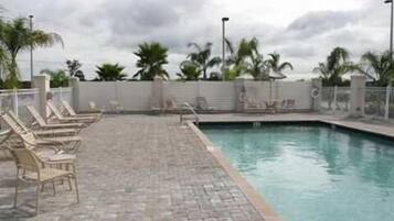 Une piscine avec des chaises longues et des palmiers en arrière-plan.