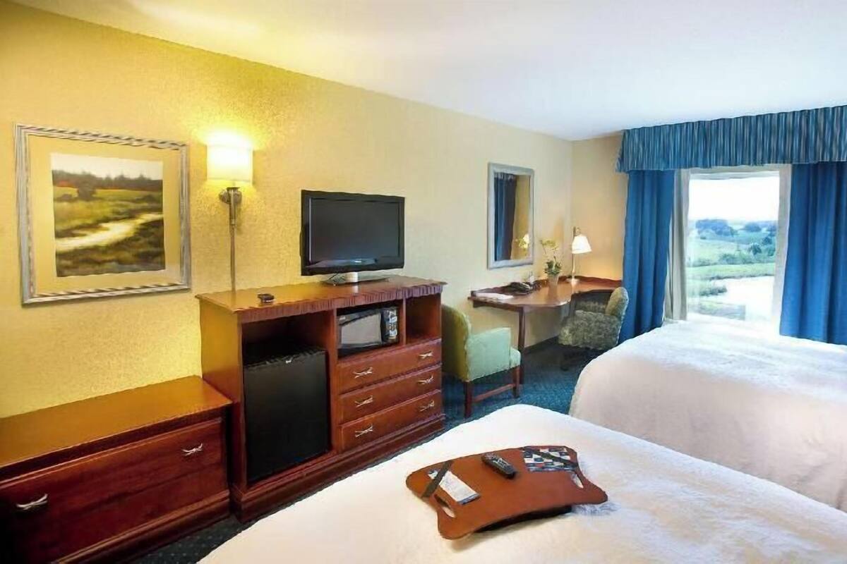 A hotel room with a bed, a desk, a television, and a window with curtains.
