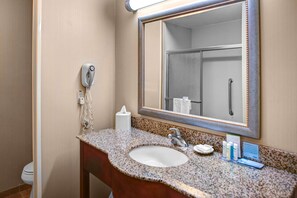 A bathroom with a granite countertop, a sink, a mirror, a towel dispenser, a hand dryer, and a toilet.