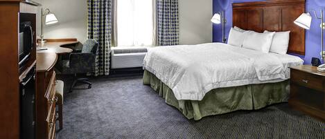 A hotel room with a bed, desk, chair, television, and a window with curtains.