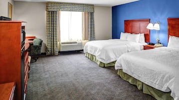 Een hotelkamer met twee bedden, een bureau, een stoel, een kaptafel en een raam met gordijnen met een patroon.