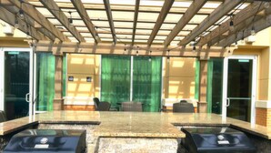 An outdoor patio with a stone countertop, two barbecue grills, wicker chairs, and a pergola with string lights. - Homewood Suites by Hilton Virginia Beach/Norfolk Airport (Virginia Beach)
