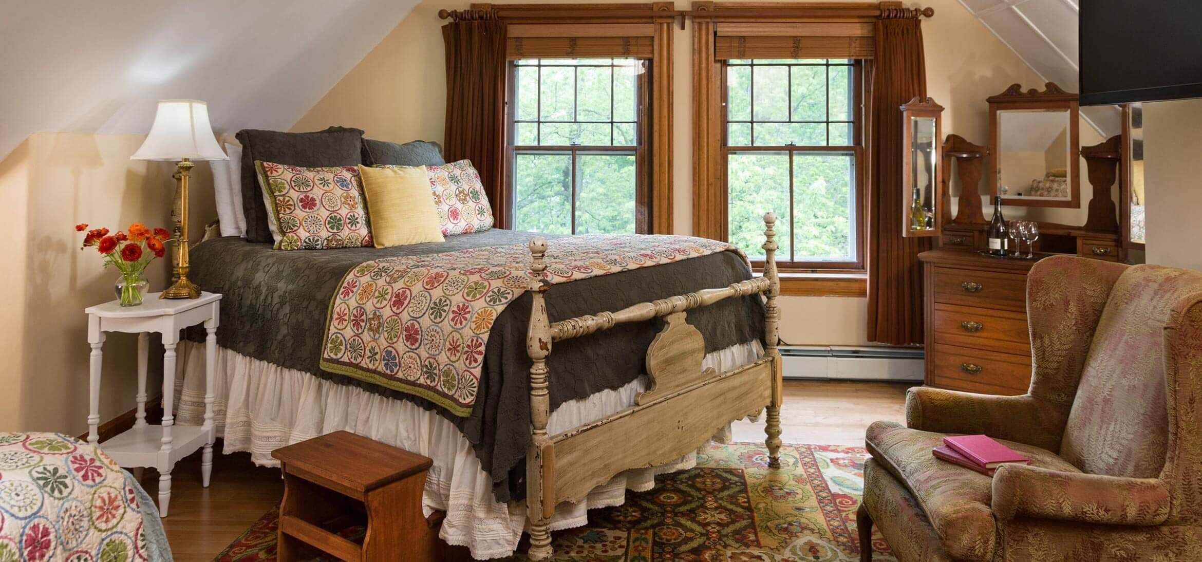 A bedroom with a large bed, a wooden dresser, a chair, and a window with curtains.