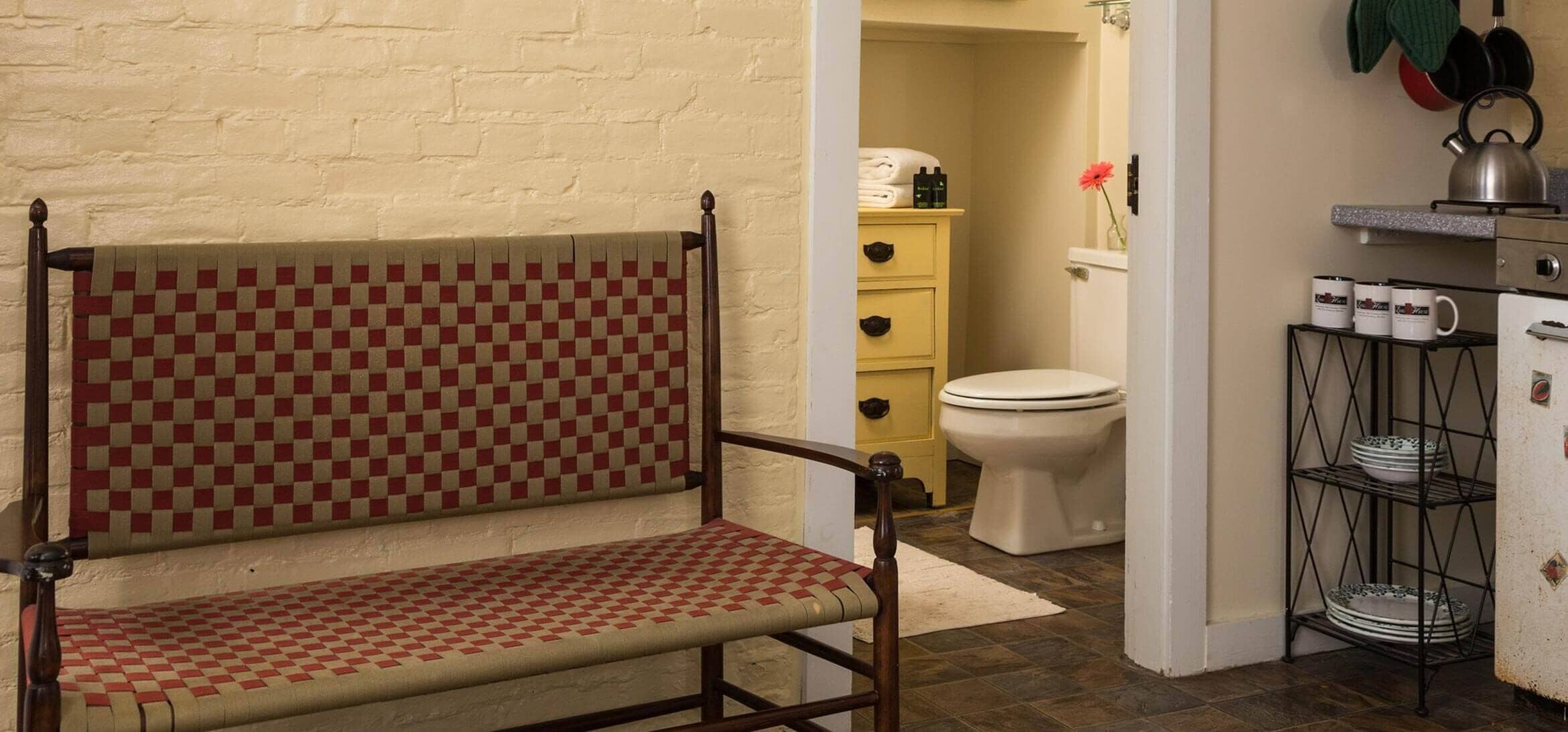 A bench with a checkered pattern, a white toilet, a yellow cabinet, and a metal shelf with plates.