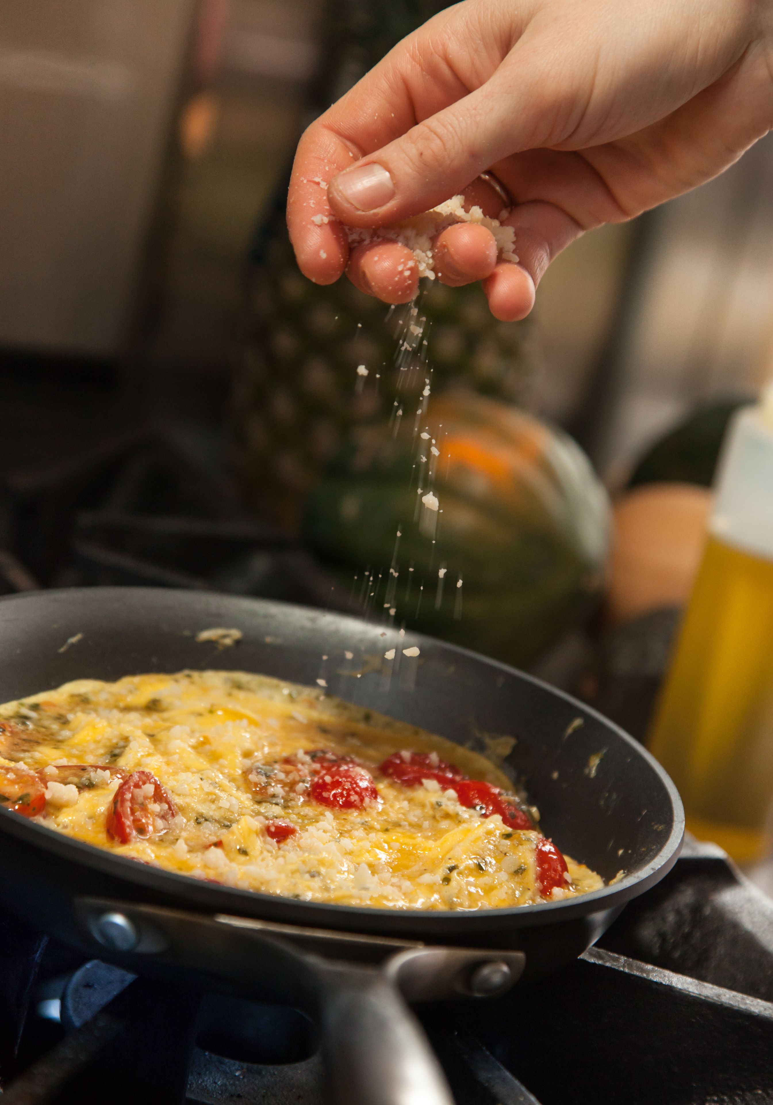 A hand sprinkling salt over a dish in a pan.