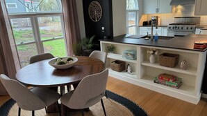 A modern kitchen with white cabinets, a central island, and a dining area with a round table and chairs. - Lang House On Main Street (Burlington)