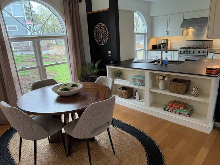 A modern kitchen with white cabinets, a central island, and a dining area with a round table and chairs.