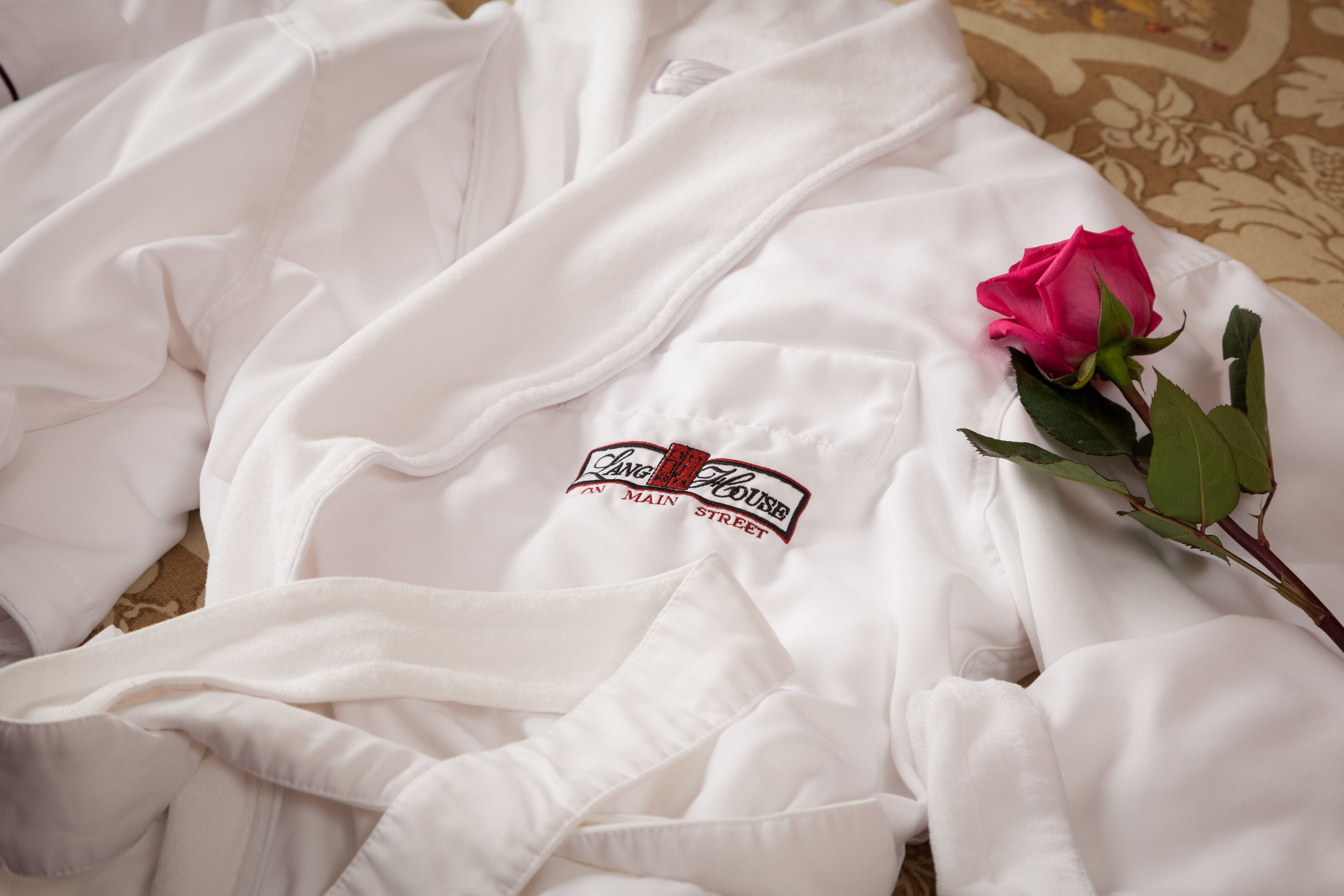 Una bata blanca con un logotipo en el pecho, una rosa rosa y una alfombra estampada.