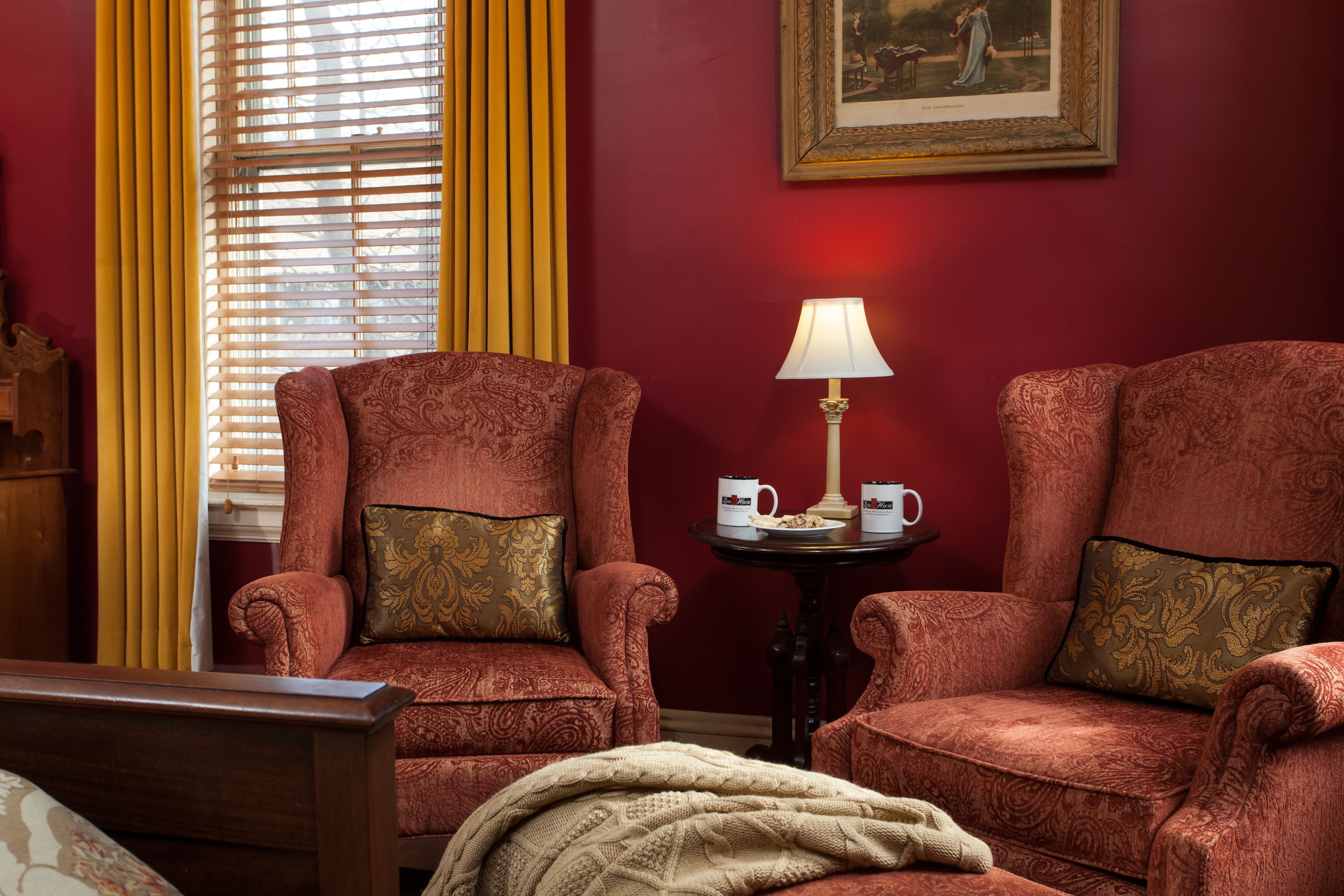 A room with two armchairs, a bedside table with a lamp, and a framed picture on the wall.