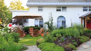 A white house with a garden patio featuring wooden chairs and a large umbrella. - Lang House On Main Street (Burlington)