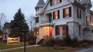 A large, white, two-story house with a steeply pitched roof, a prominent tower with a weathervane, and a red door on the front porch. - Lang House On Main Street (Burlington)