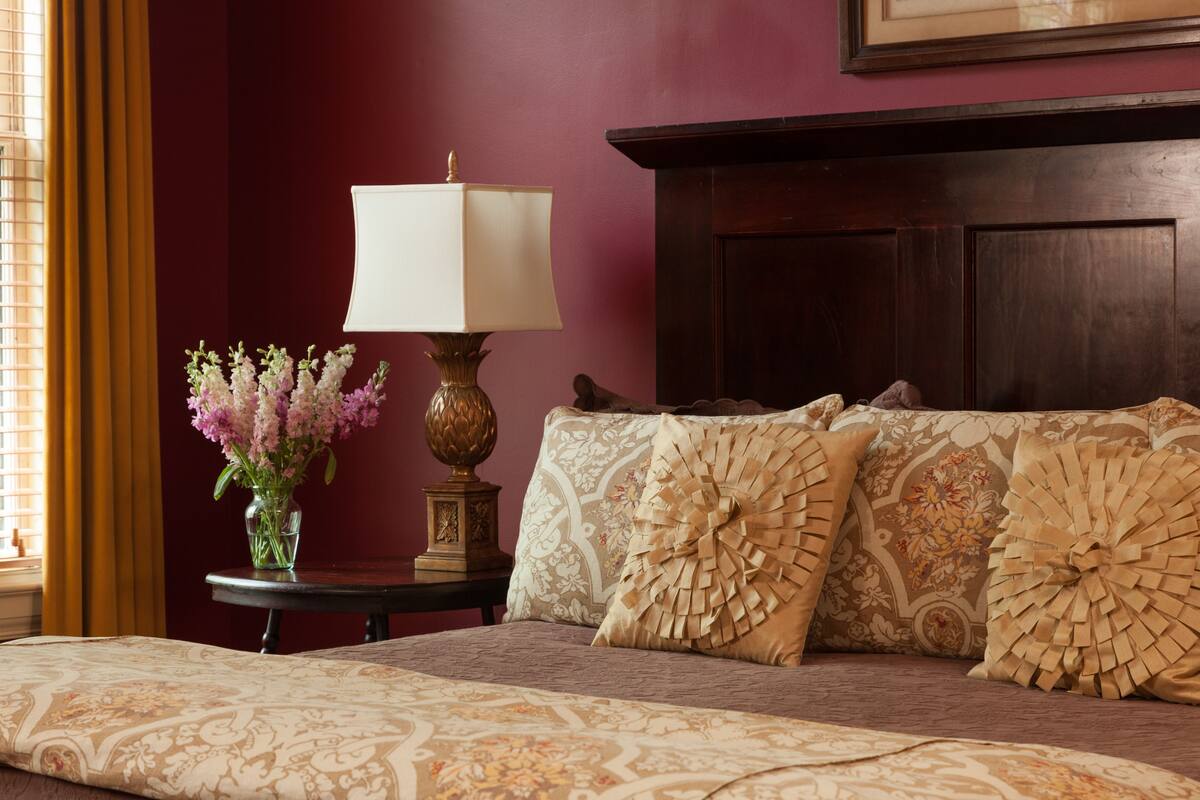 A neatly made bed with patterned bedding, a decorative lamp, and a vase of flowers on a bedside table.