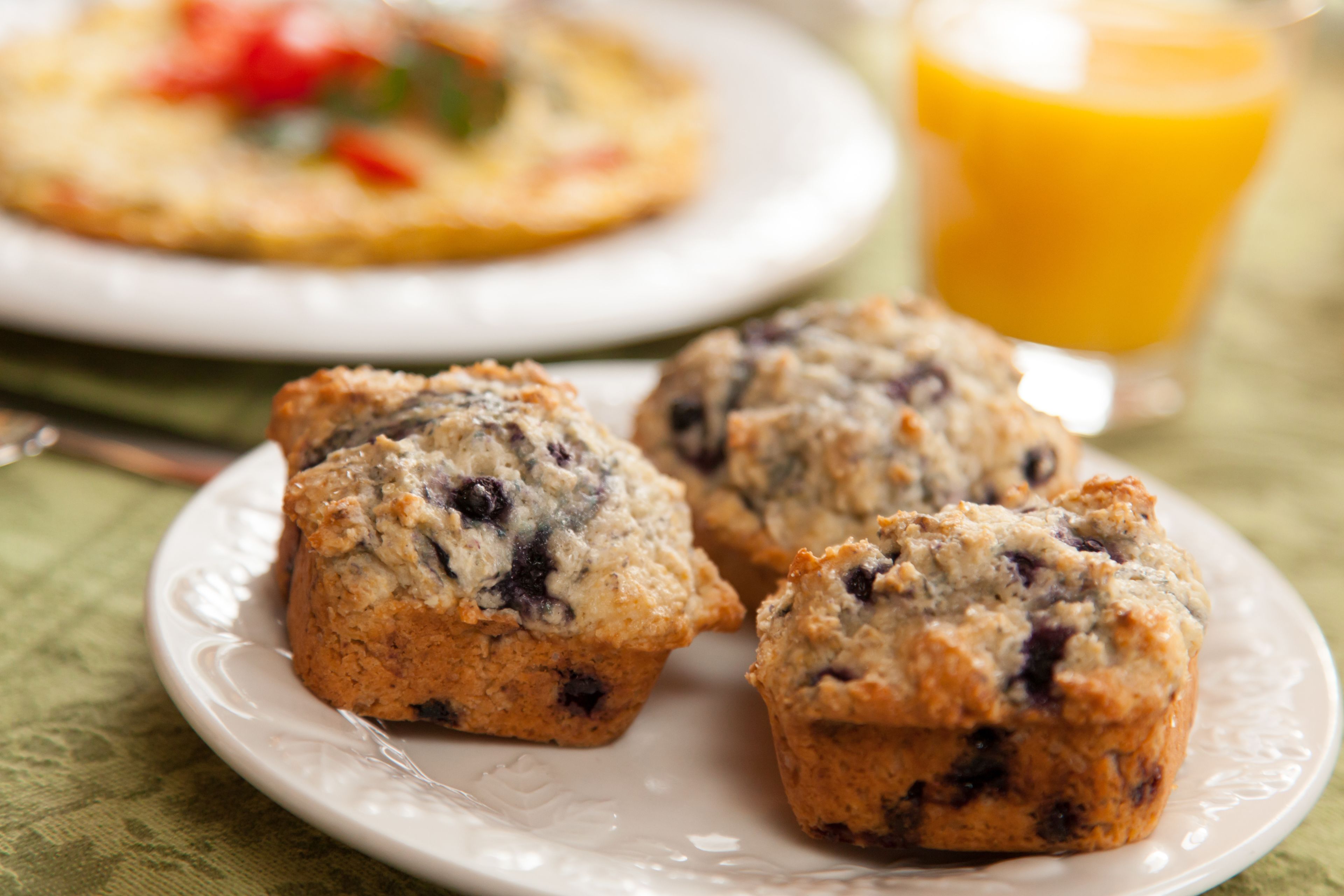 Un plato con tres muffins y un vaso de jugo de naranja sobre una mesa.