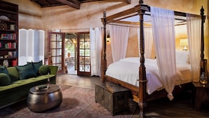 A four-poster bed with white linens, a green sofa, a wooden coffee table, and a bookshelf with books. - Korakia Pensione (Palm Springs)