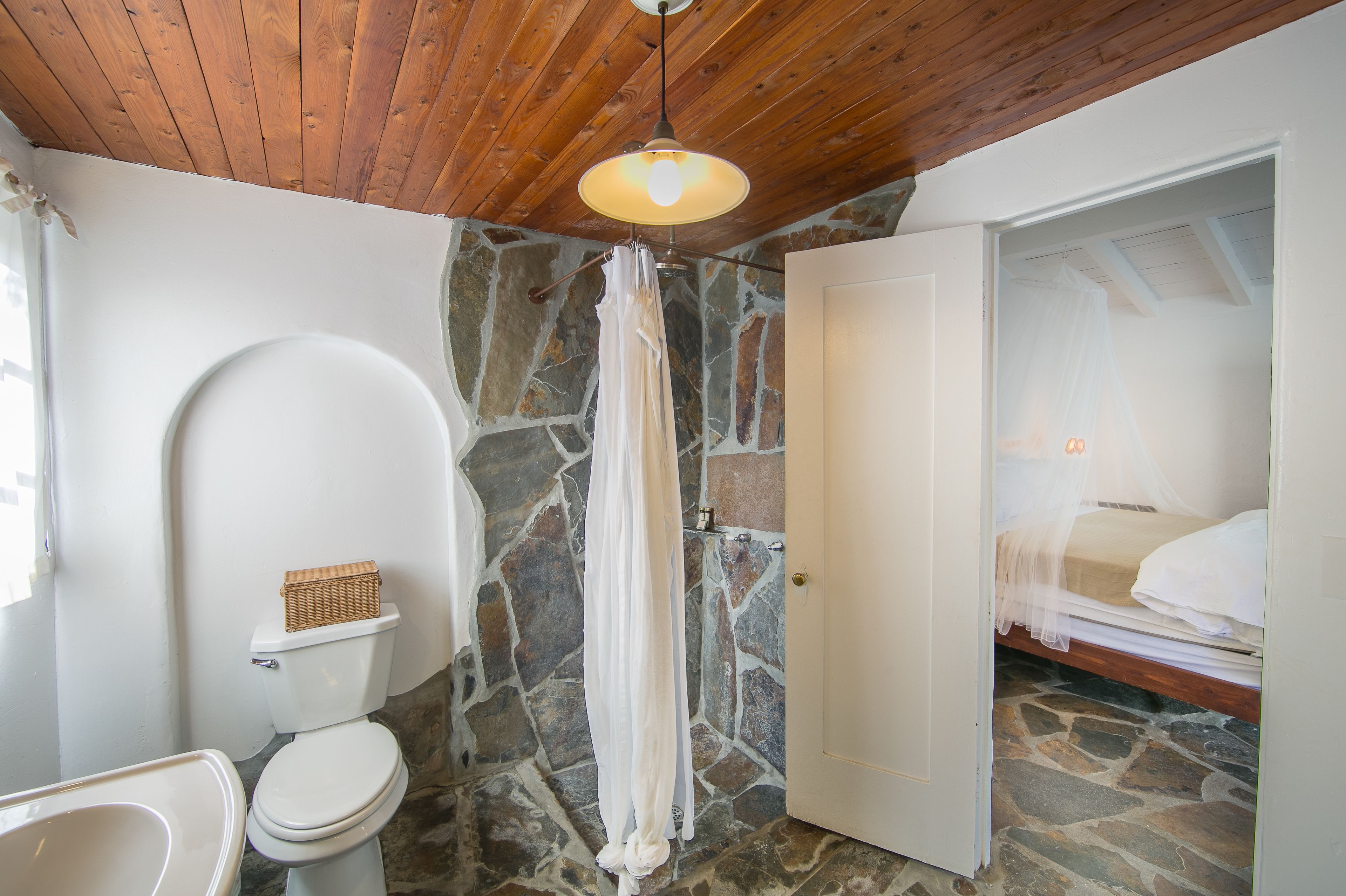 A bathroom with a stone wall, a wooden ceiling, a white toilet, and a shower curtain.