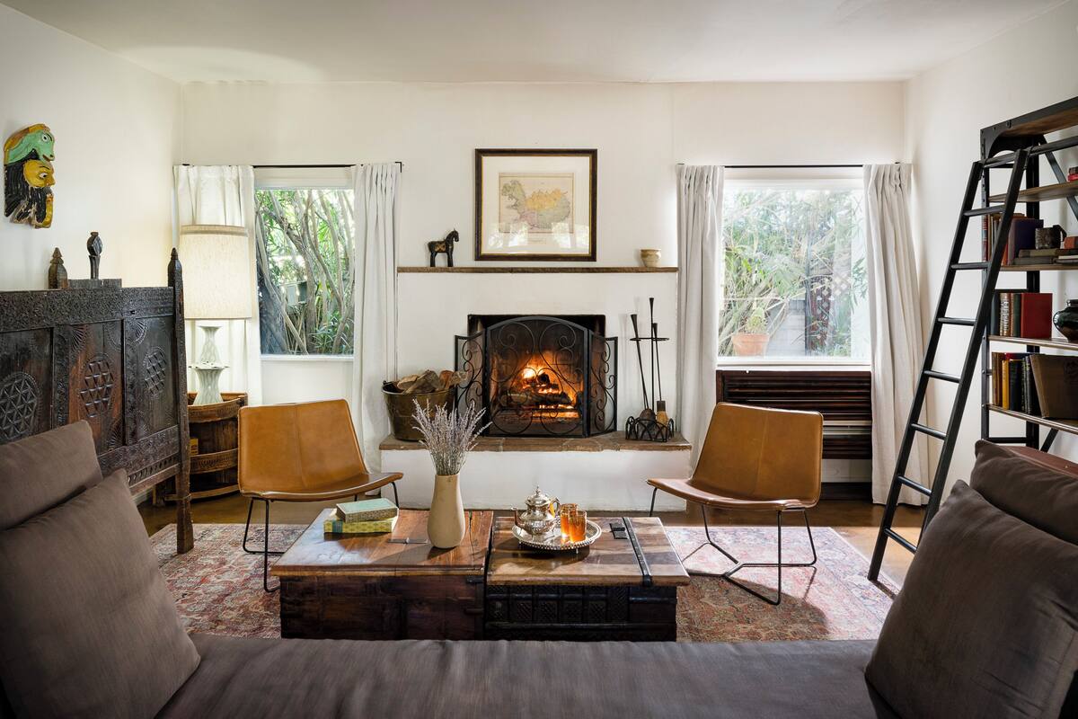 A cozy living room with a fireplace, two armchairs, a coffee table with a tray, and a bookshelf.