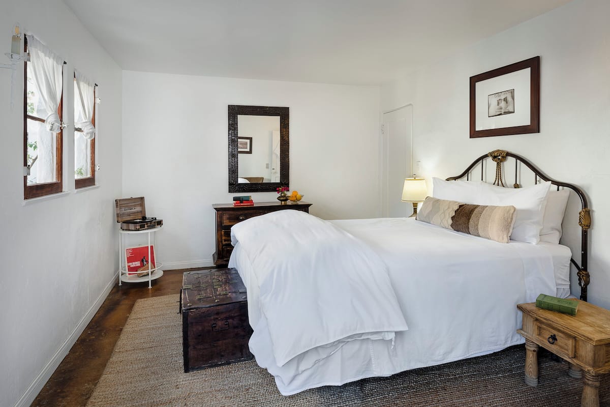 A bedroom with a large bed, a wooden nightstand, a dresser, a mirror, and a framed picture on the wall.