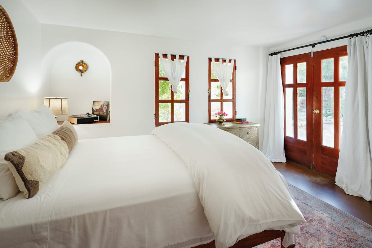 A spacious bedroom with a large bed, two windows with curtains, a dresser, and a rug.