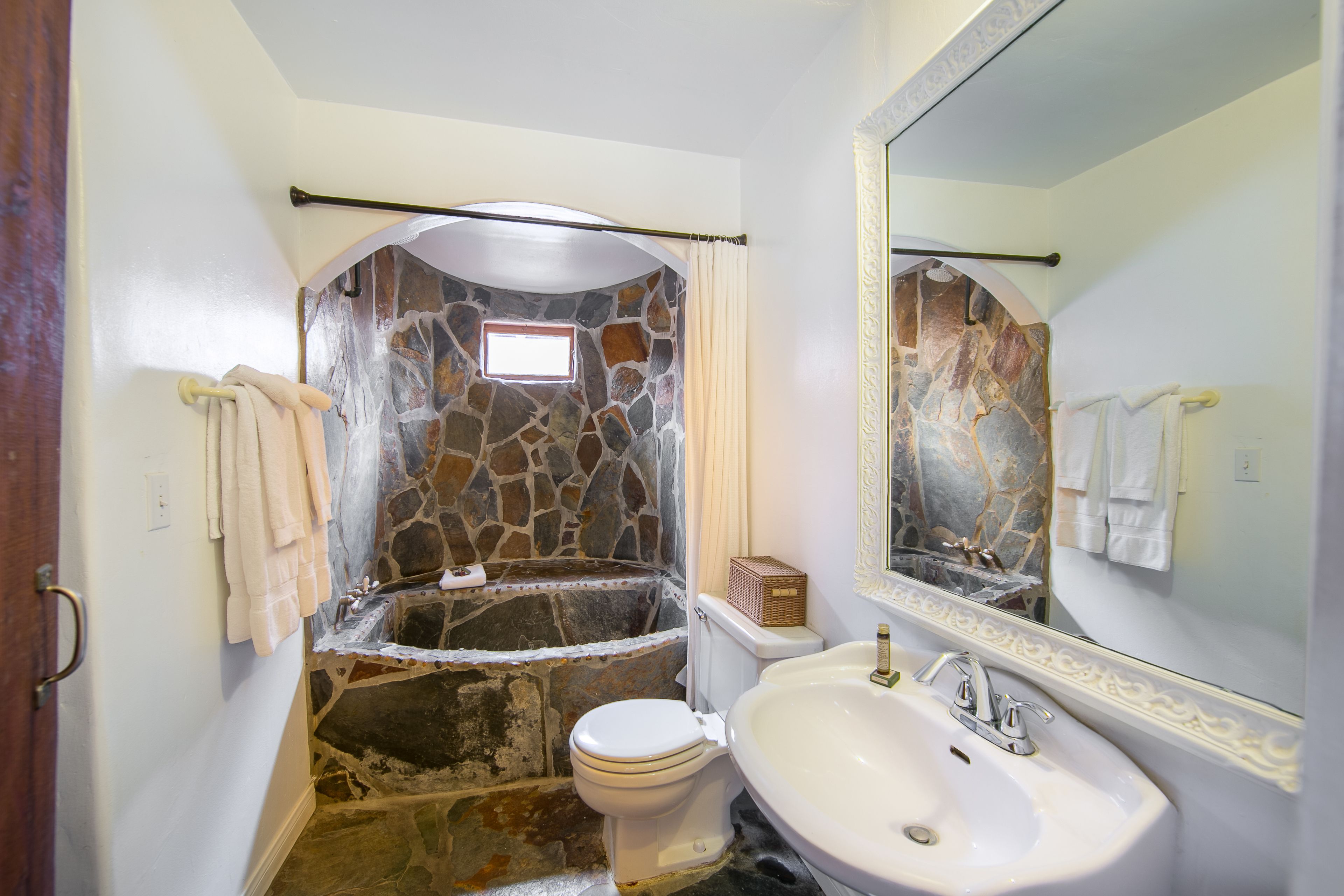 A bathroom with a stone wall, a bathtub, a toilet, and a sink.