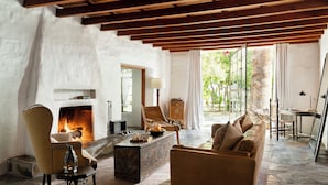 A cozy living room with a fireplace, comfortable seating, and a view of greenery outside. - Korakia Pensione (Palm Springs)