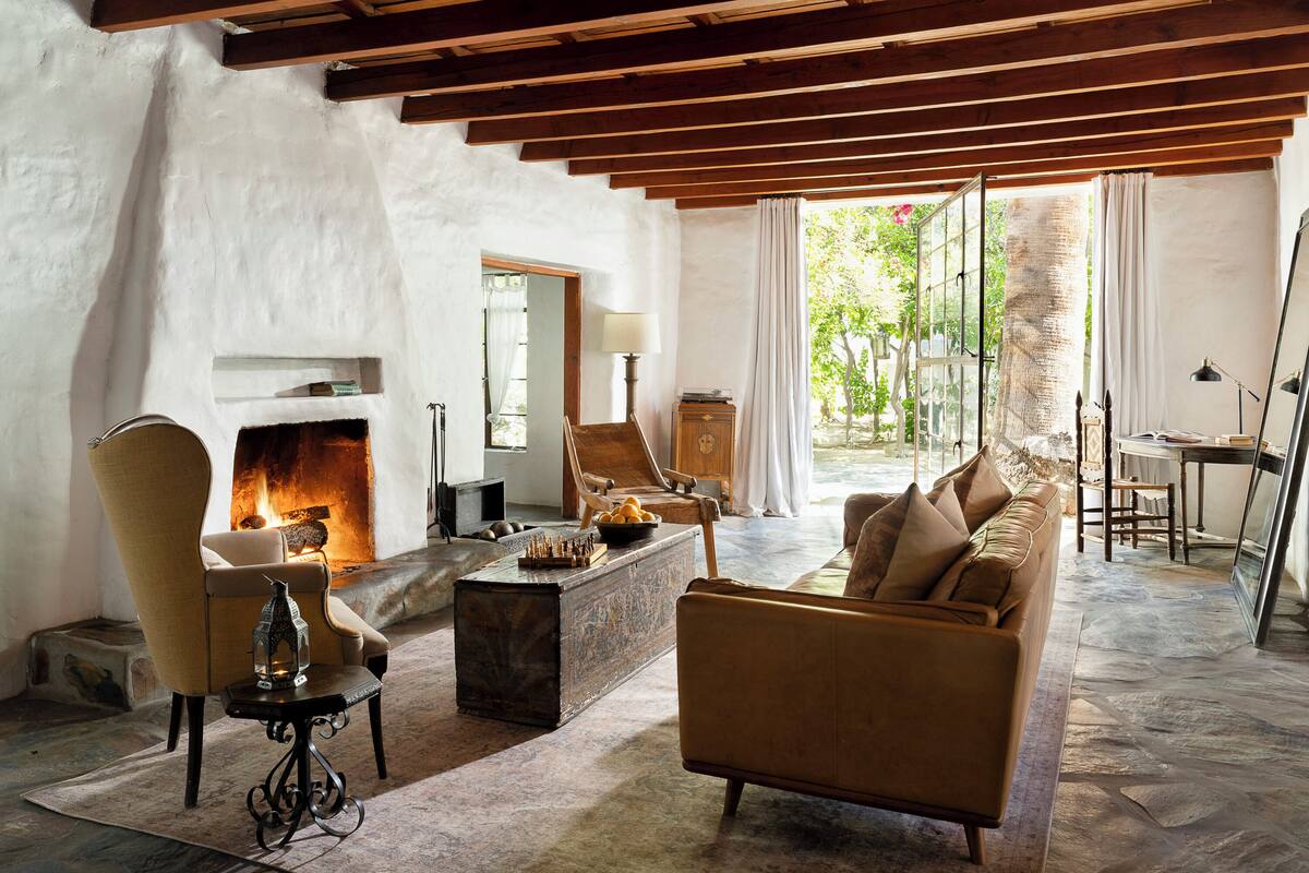 A cozy living room with a fireplace, comfortable seating, and a view of greenery outside.