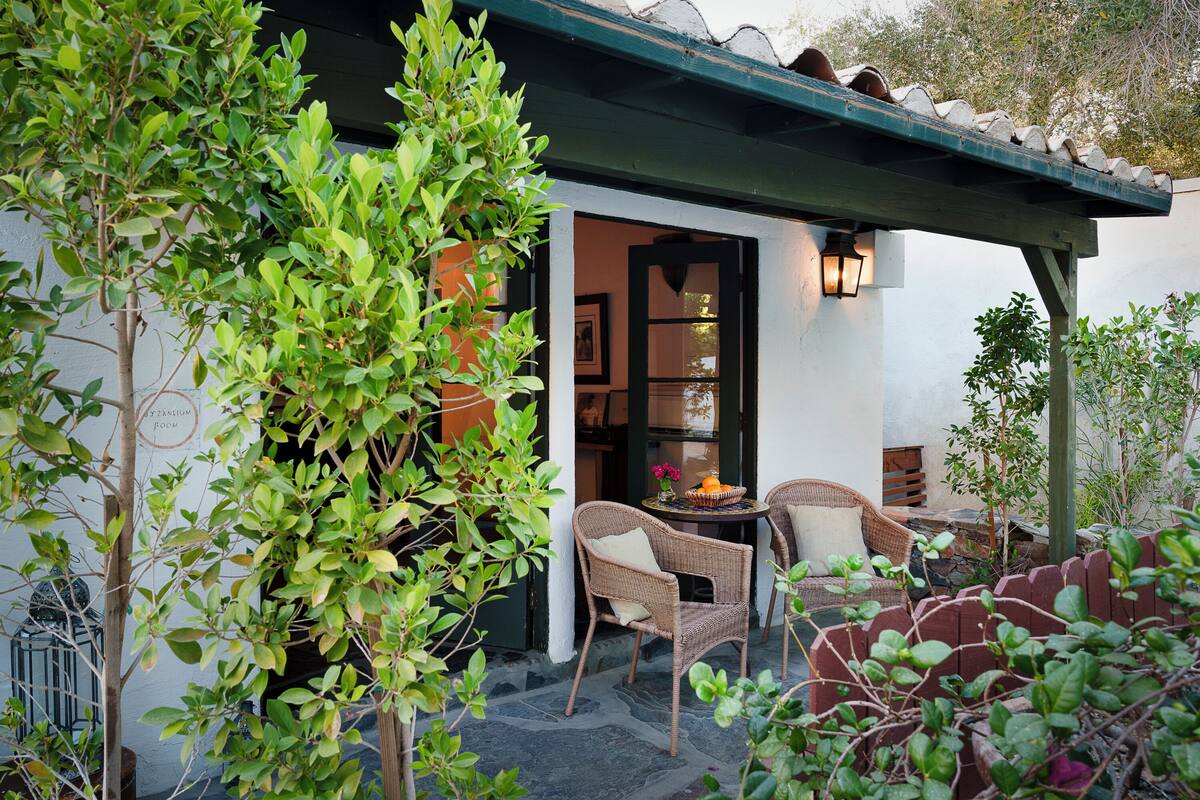A cozy outdoor seating area with wicker chairs and a table, surrounded by lush greenery and a pergola.