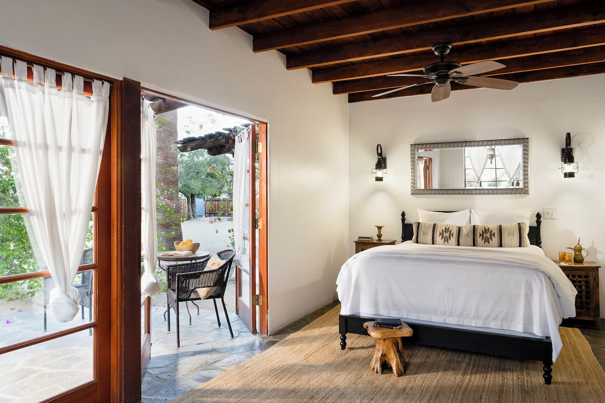 A bedroom with a large bed, a ceiling fan, a mirror, and a small table with chairs.