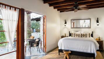A bedroom with a large bed, a ceiling fan, a mirror, and a small table with chairs.