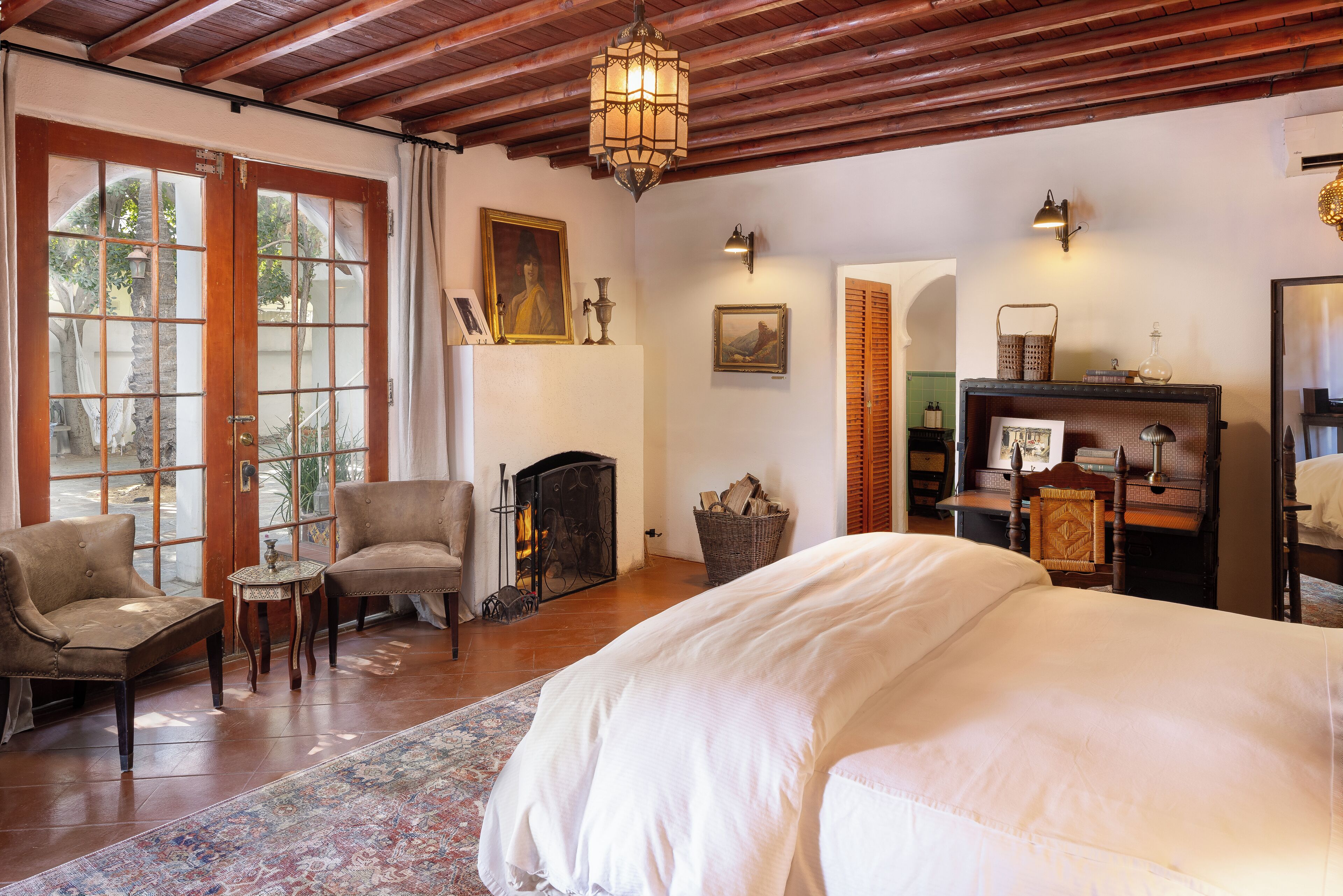 A room with a large bed, two armchairs, a fireplace, and a wooden ceiling.