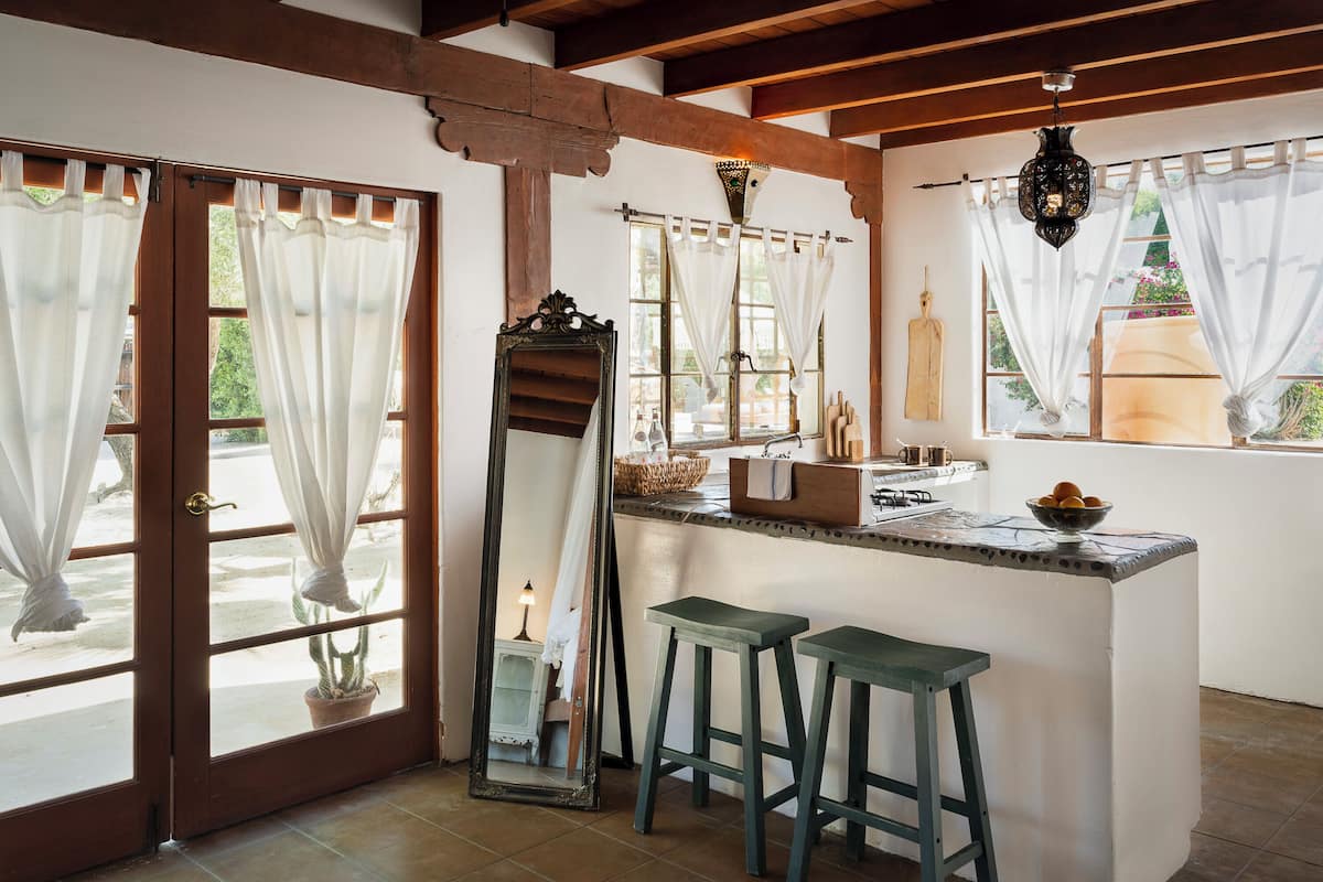 A kitchen with a central island, two stools, a large mirror, and a hanging light fixture.