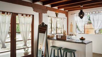 A kitchen with a central island, two stools, a large mirror, and a hanging light fixture.
