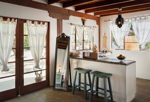A kitchen with a central island, two stools, a large mirror, and a hanging light fixture.