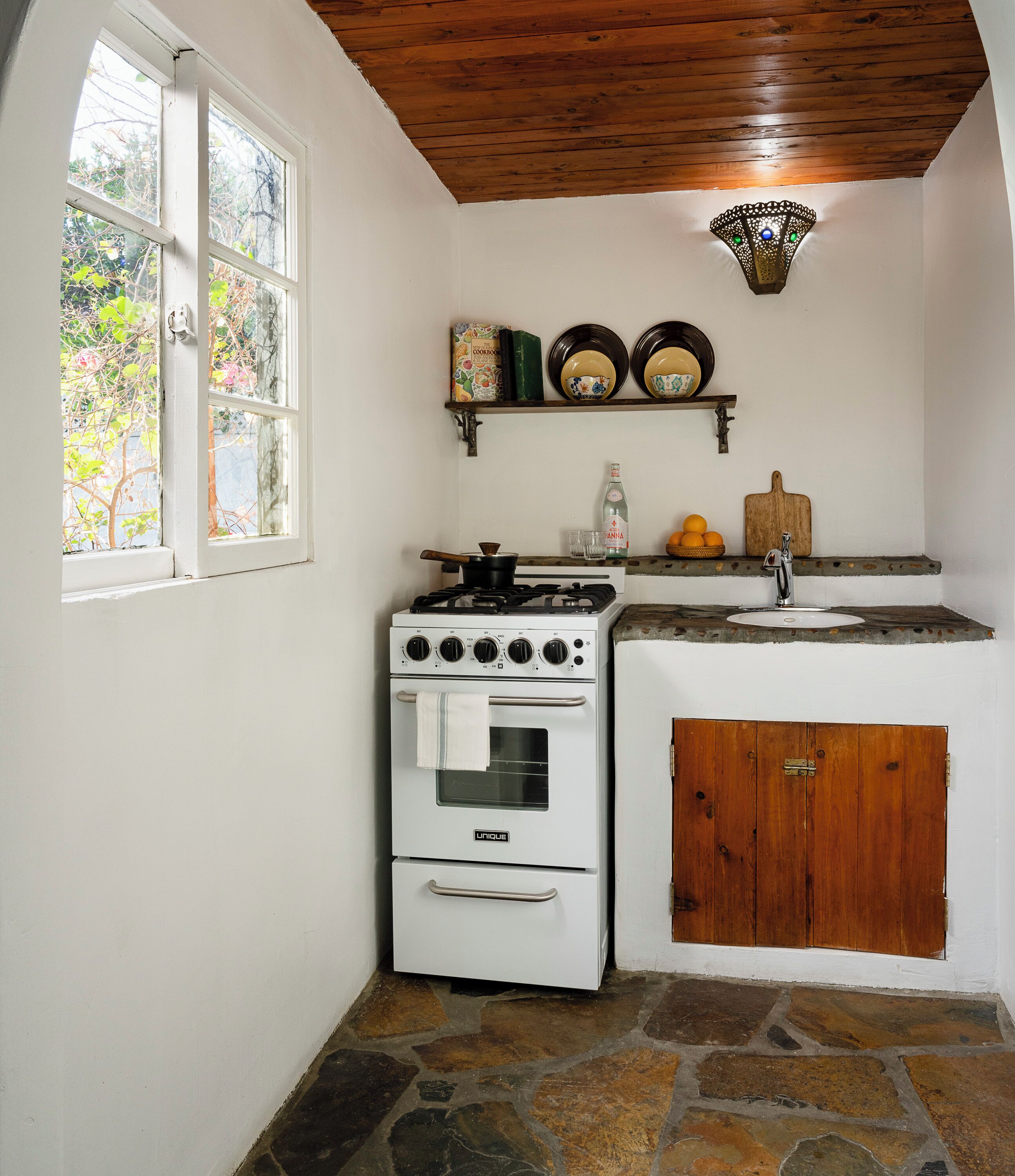 A kitchen with a white stove, a sink, and a wooden cabinet.