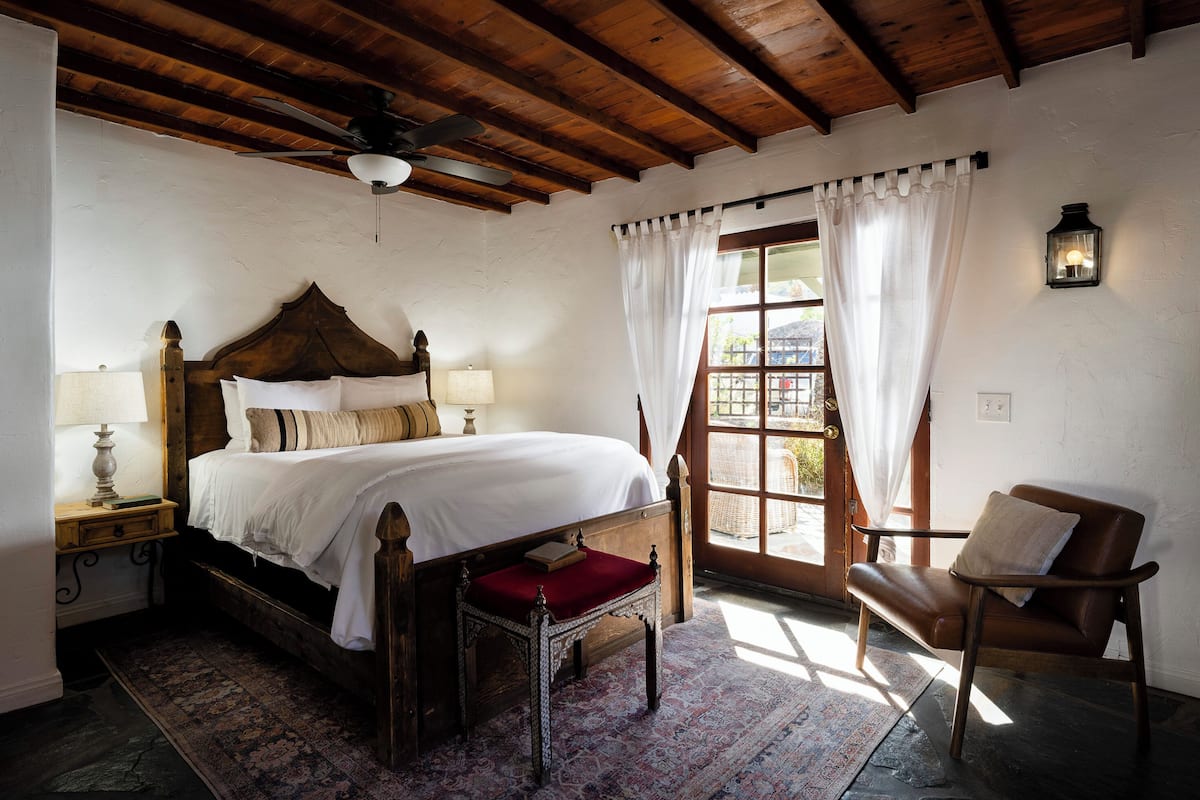 A bedroom with a wooden bed, a nightstand, a chair, a window with curtains, and a ceiling fan.