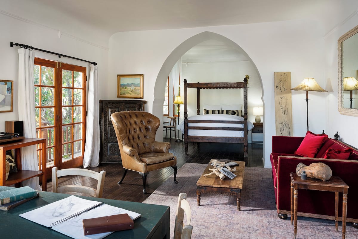 A traditional room with a large bed, a leather armchair, a wooden desk, and a red sofa.