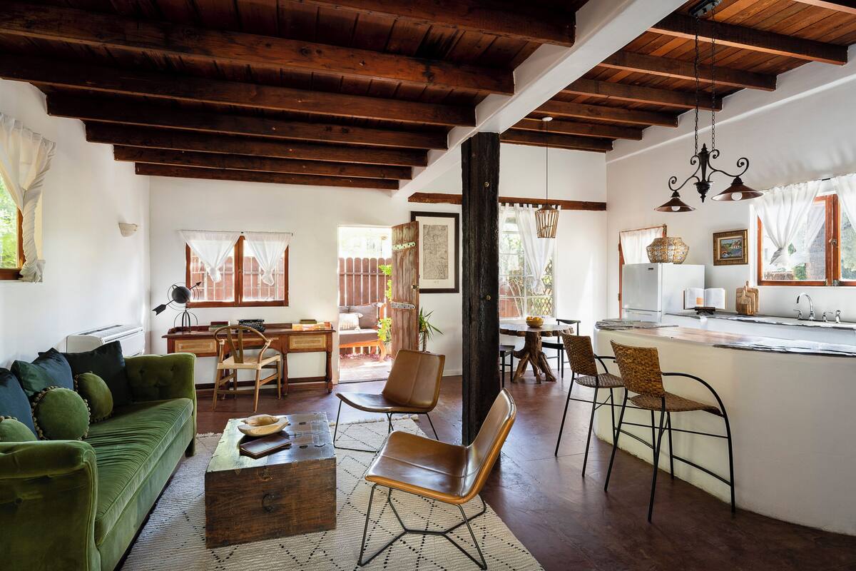 A spacious living area with a green sofa, wooden coffee table, and a kitchen area with a bar counter and seating.