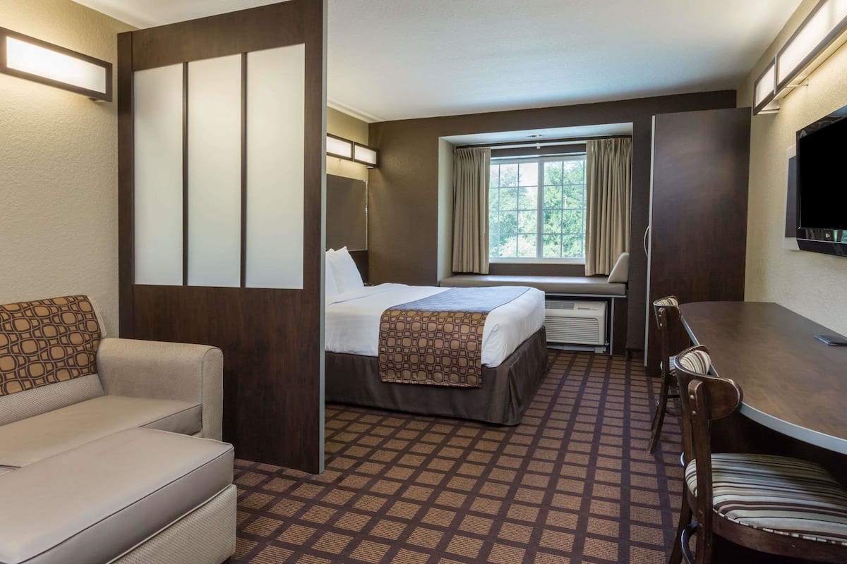 A hotel room with a bed, a desk, a chair, a sofa, and a TV.