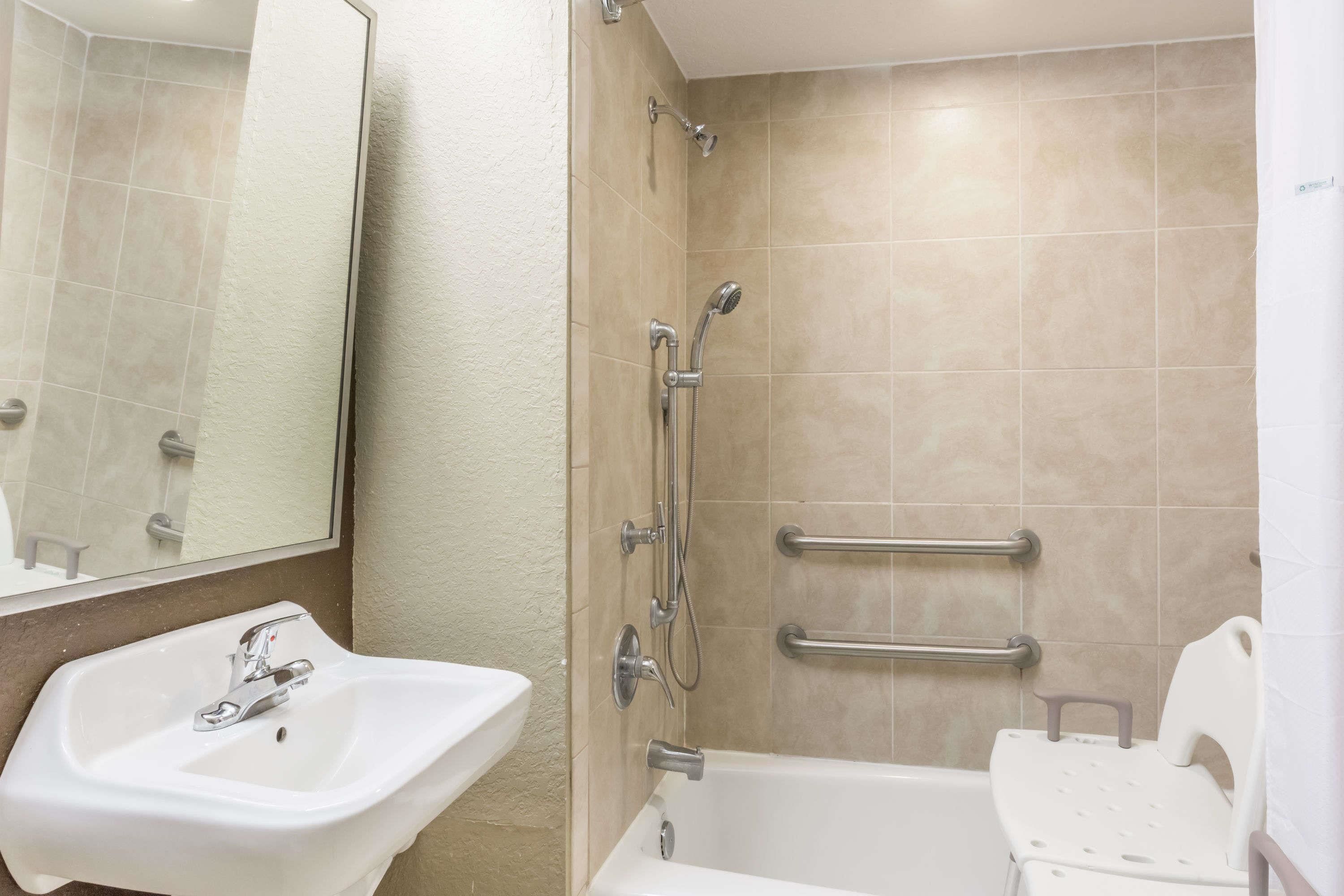 A bathroom with a sink, mirror, shower, and grab bars.