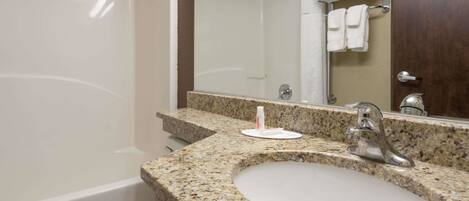 A bathroom with a granite countertop sink, a mirror, a shower, and a toilet.