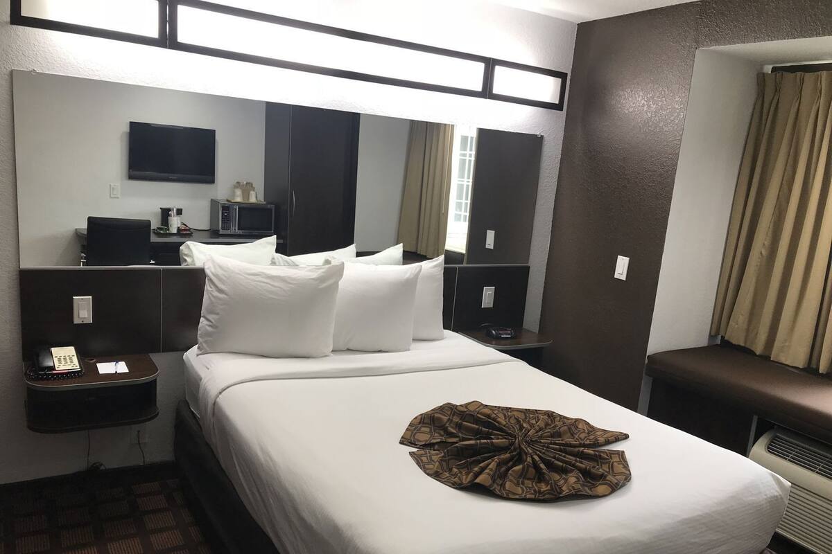 A hotel room with a bed, a desk with a telephone, a microwave, a flat-screen TV, and a large mirror.