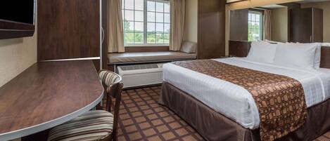 A hotel room with a bed, a desk, a chair, a window with curtains, and a view of greenery outside.