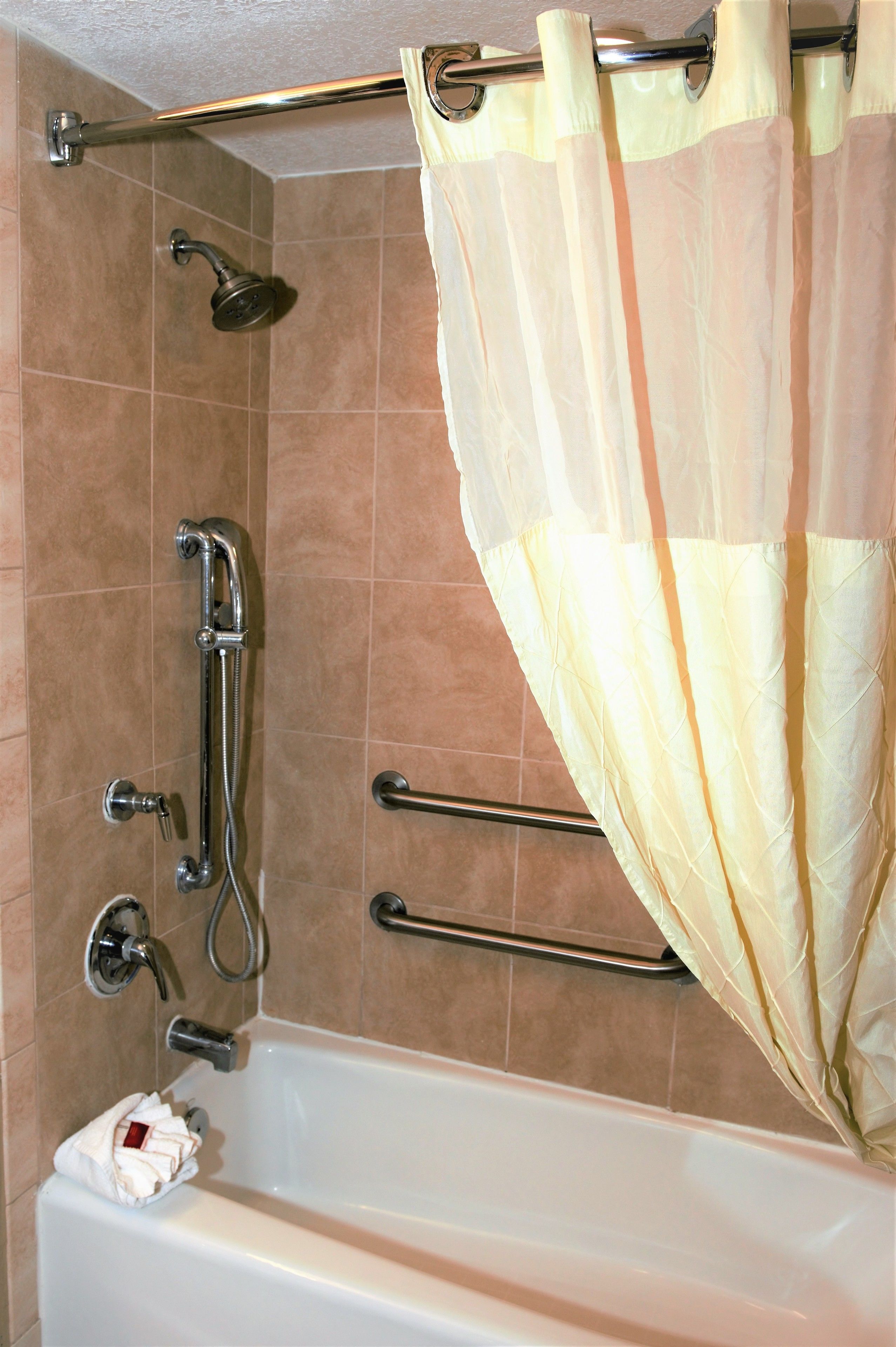 Un baño con bañera, ducha e inodoro. Hay barras de apoyo instaladas cerca de la bañera y la ducha.