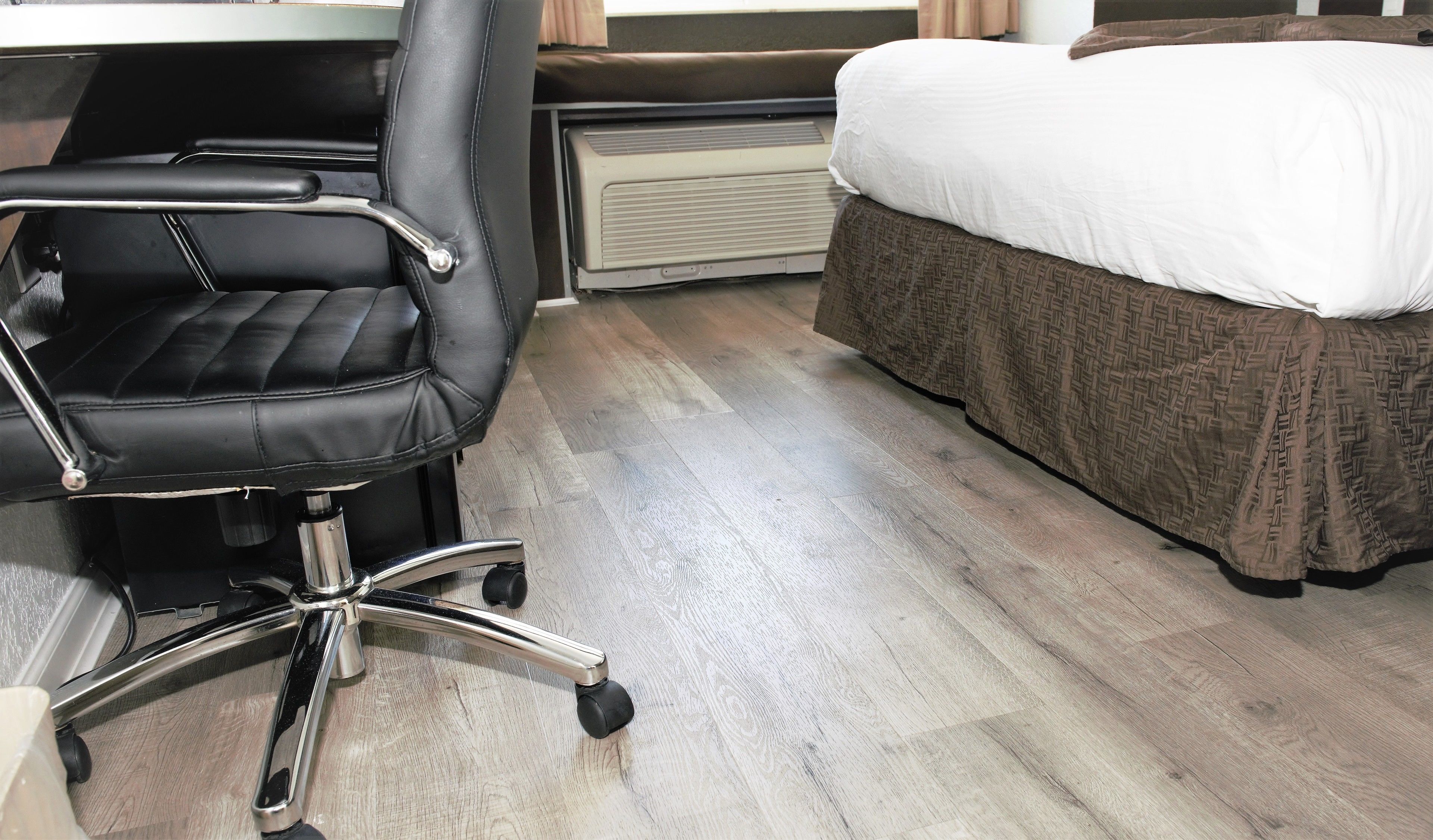 A hotel room with a black office chair, a bed with a patterned bedspread, and a radiator.