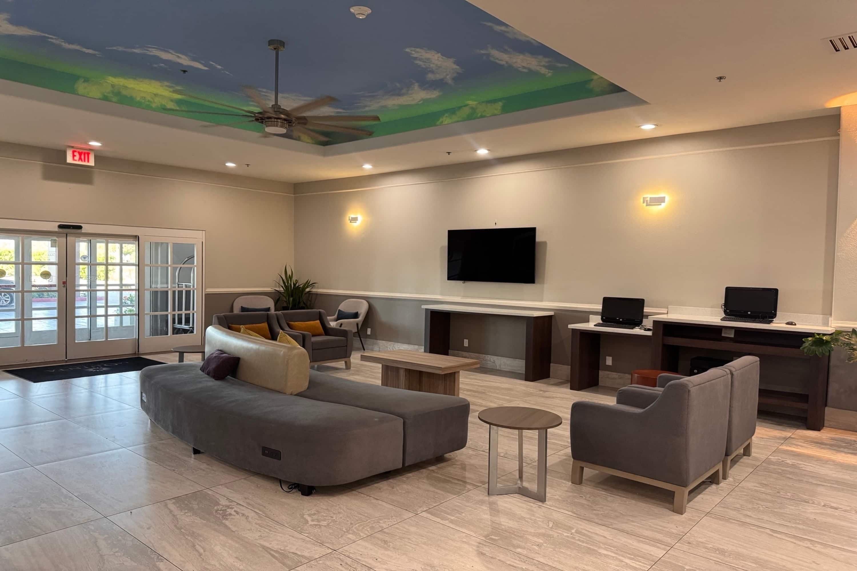 A spacious lobby with a ceiling mural, seating area, and a reception desk with computers.