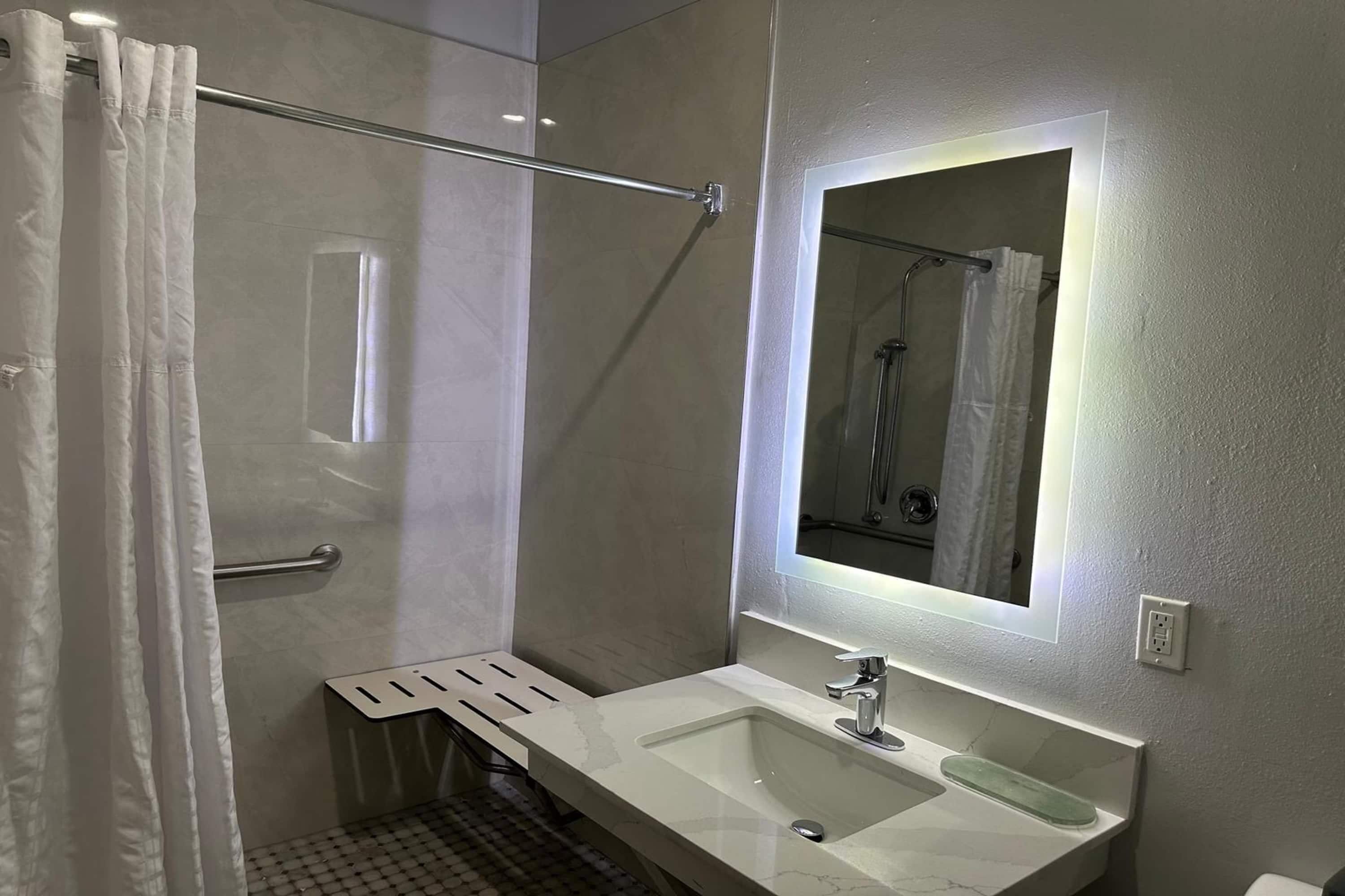 Une salle de bain moderne avec une douche à parois de verre, un lavabo blanc avec un miroir au-dessus et un porte-serviettes.