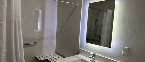 Un baño moderno con cabina de ducha de vidrio, un lavabo blanco con espejo y un perchero para toallas.